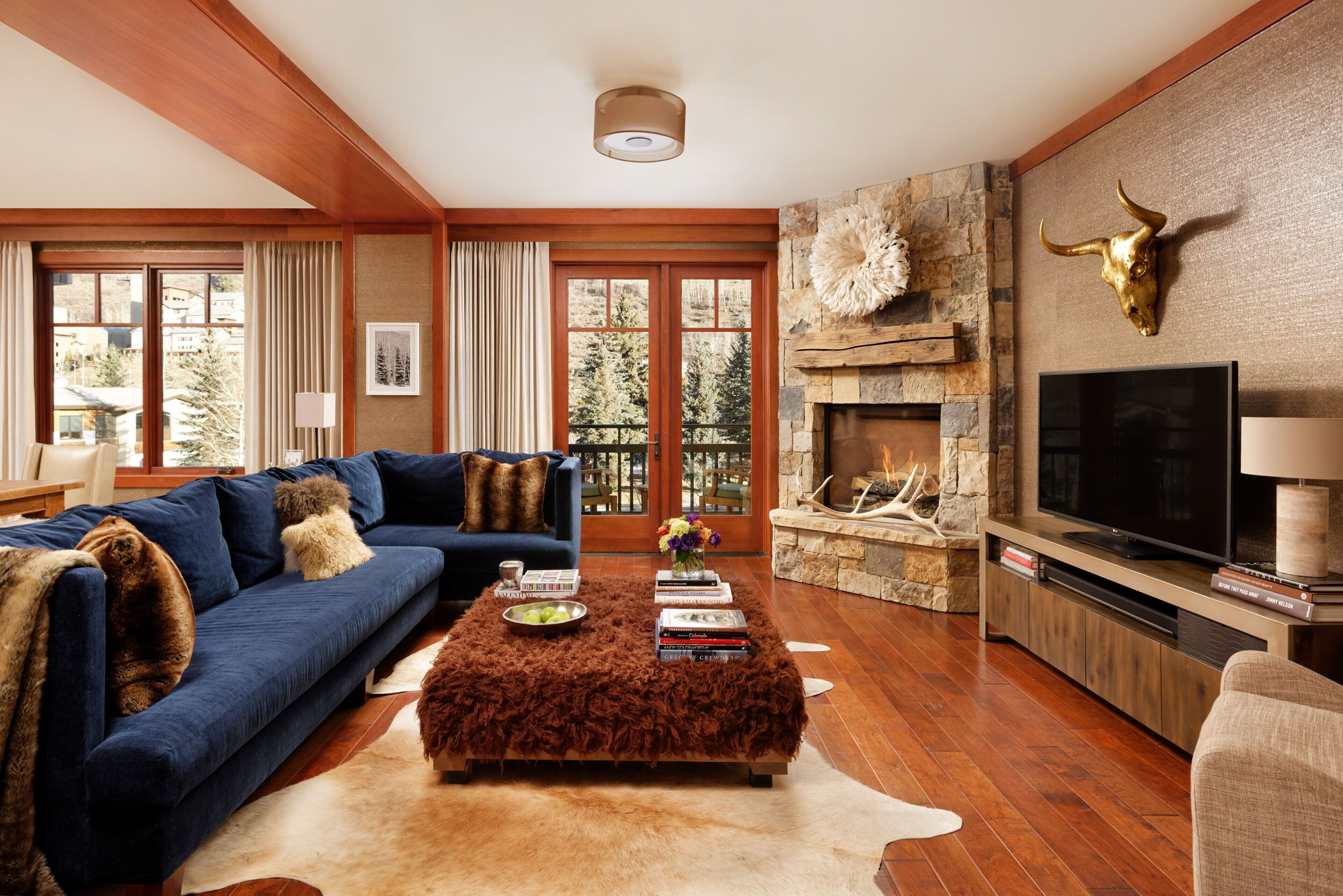 Un salon avec un canapé bleu, un pouf marron, une cheminée en pierre et une tête de taureau fixée au mur.