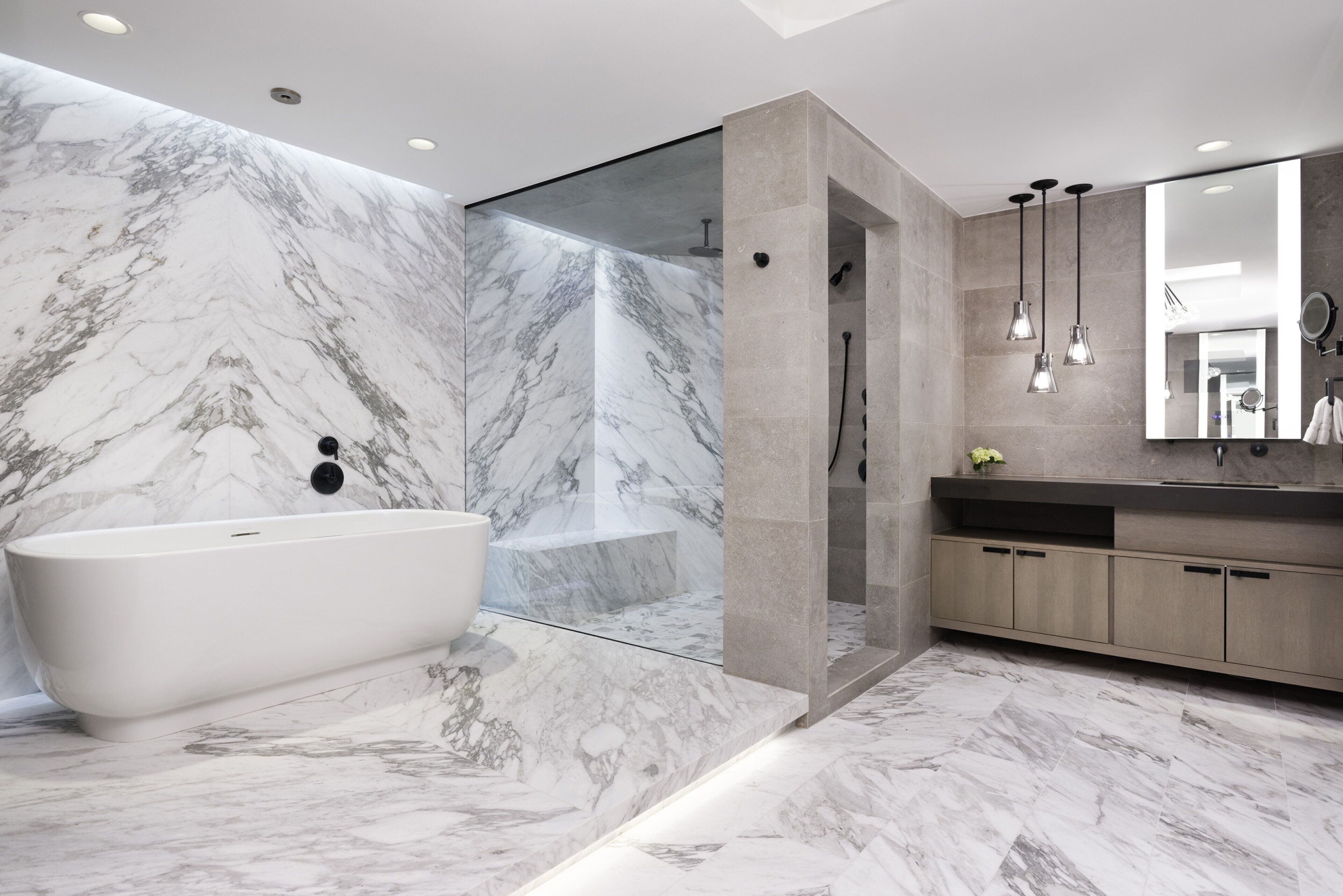 A modern bathroom with a marble wall, a freestanding bathtub, a walk-in shower, and a large mirror above the sink.