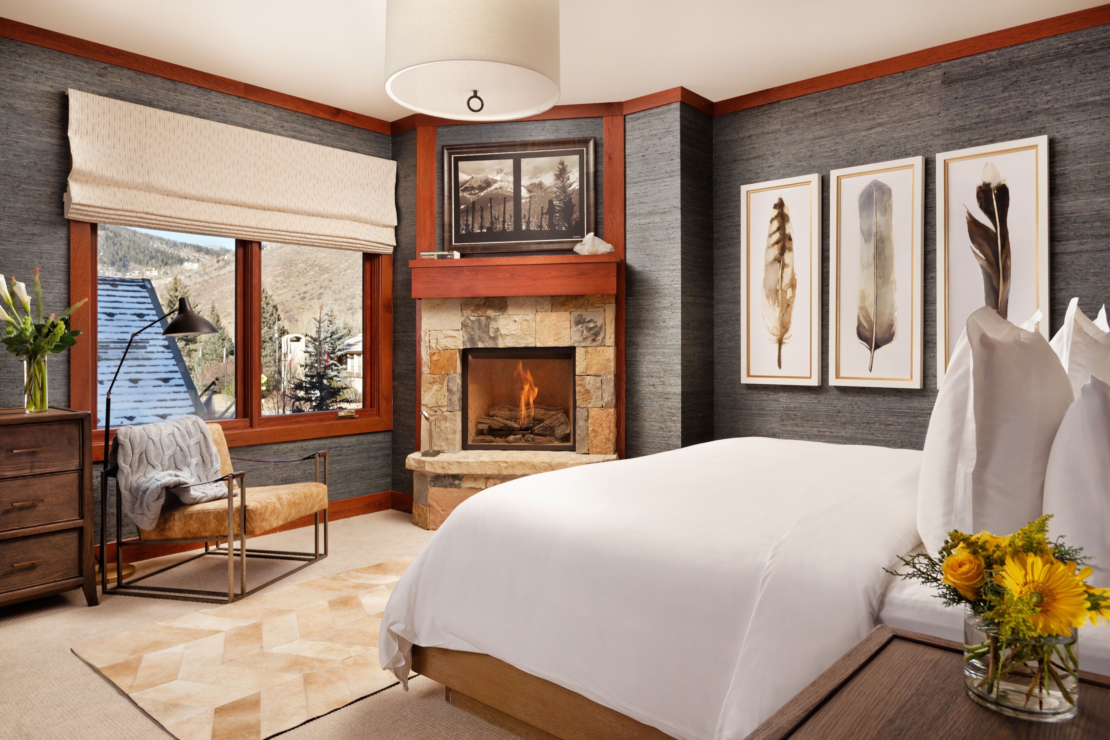 A bedroom with a stone fireplace, a bed, a chair, and artwork on the walls.