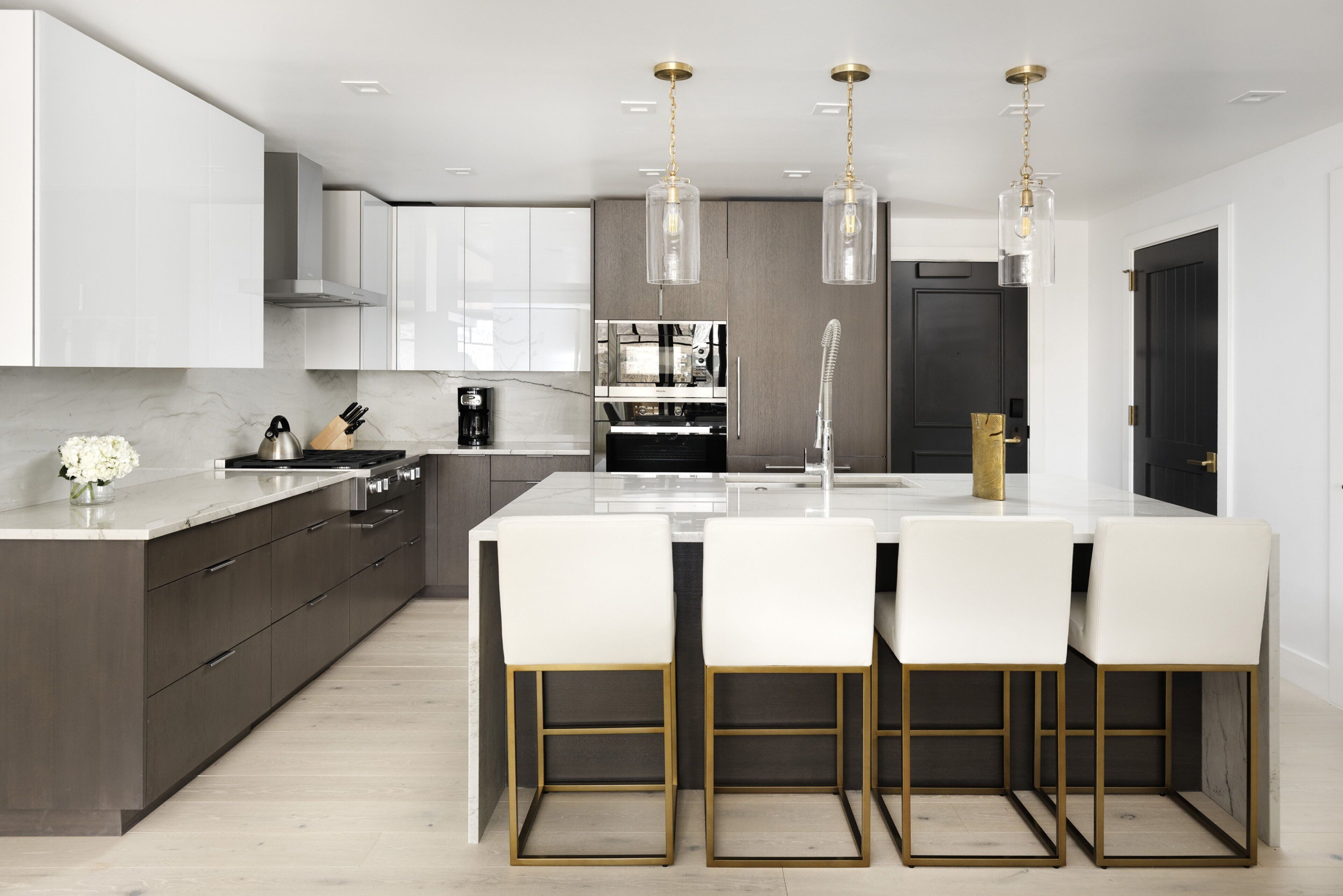 A modern kitchen with white cabinetry, a central island with bar stools, and pendant lighting.