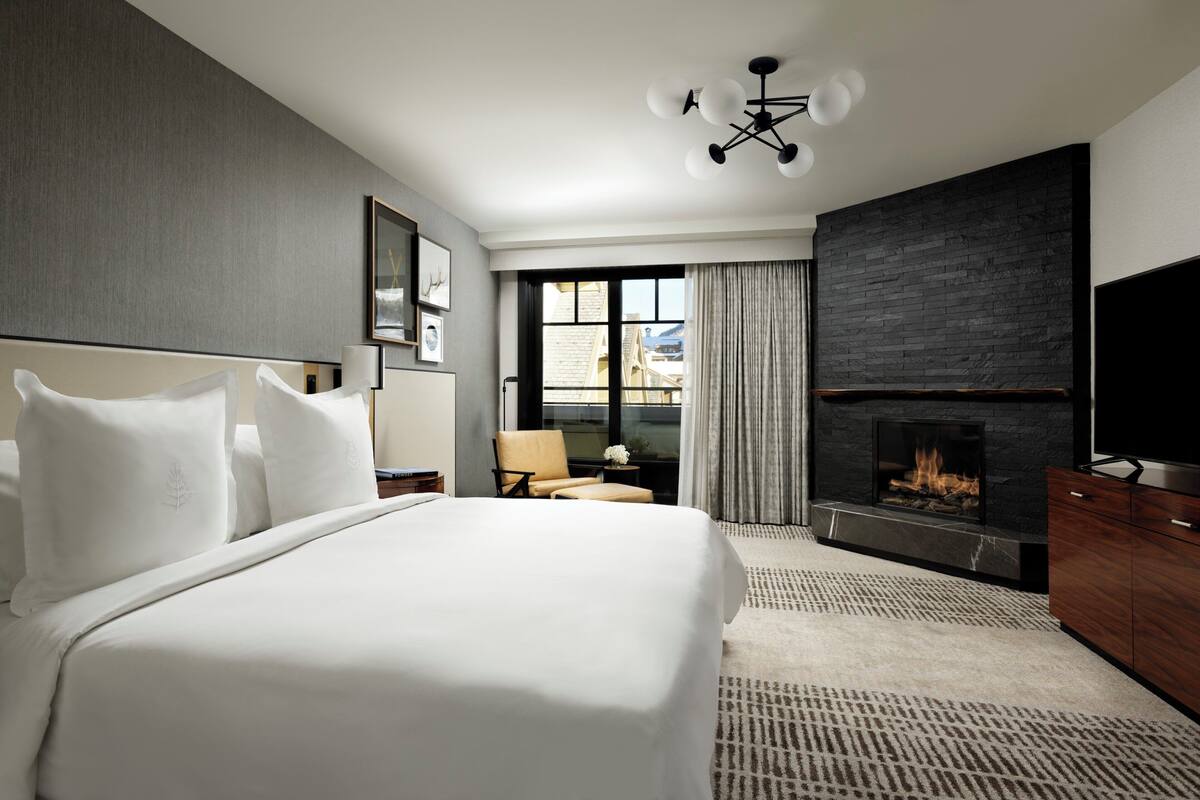 Ein modernes Hotelzimmer mit einem großen Bett, einem Kamin, einem Fernseher und Blick auf die Stadt durch das Fenster.