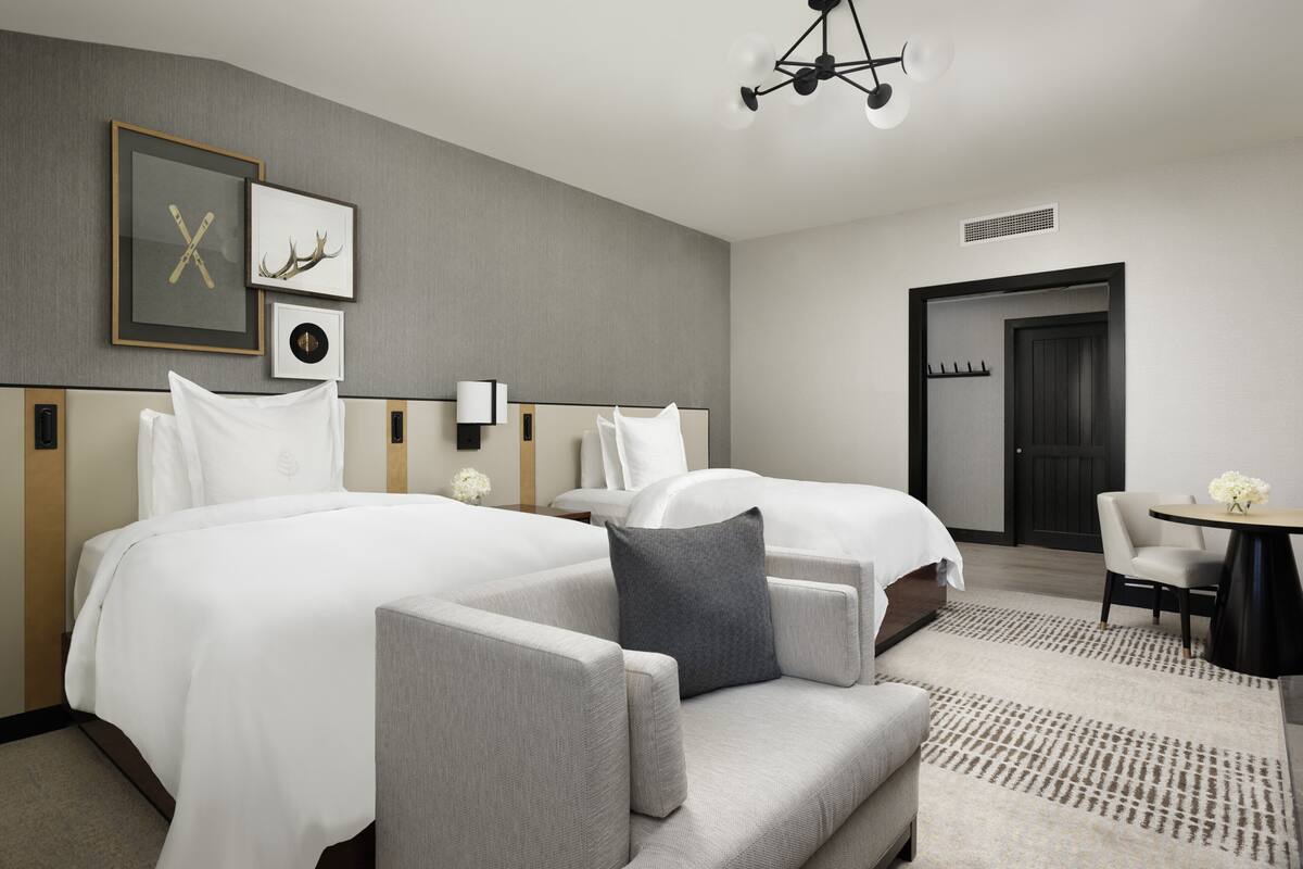 Ein Hotelzimmer mit zwei Betten, einem Sofa, einem kleinen Tisch mit Blumen und einer Tür zu einem weiteren Raum.