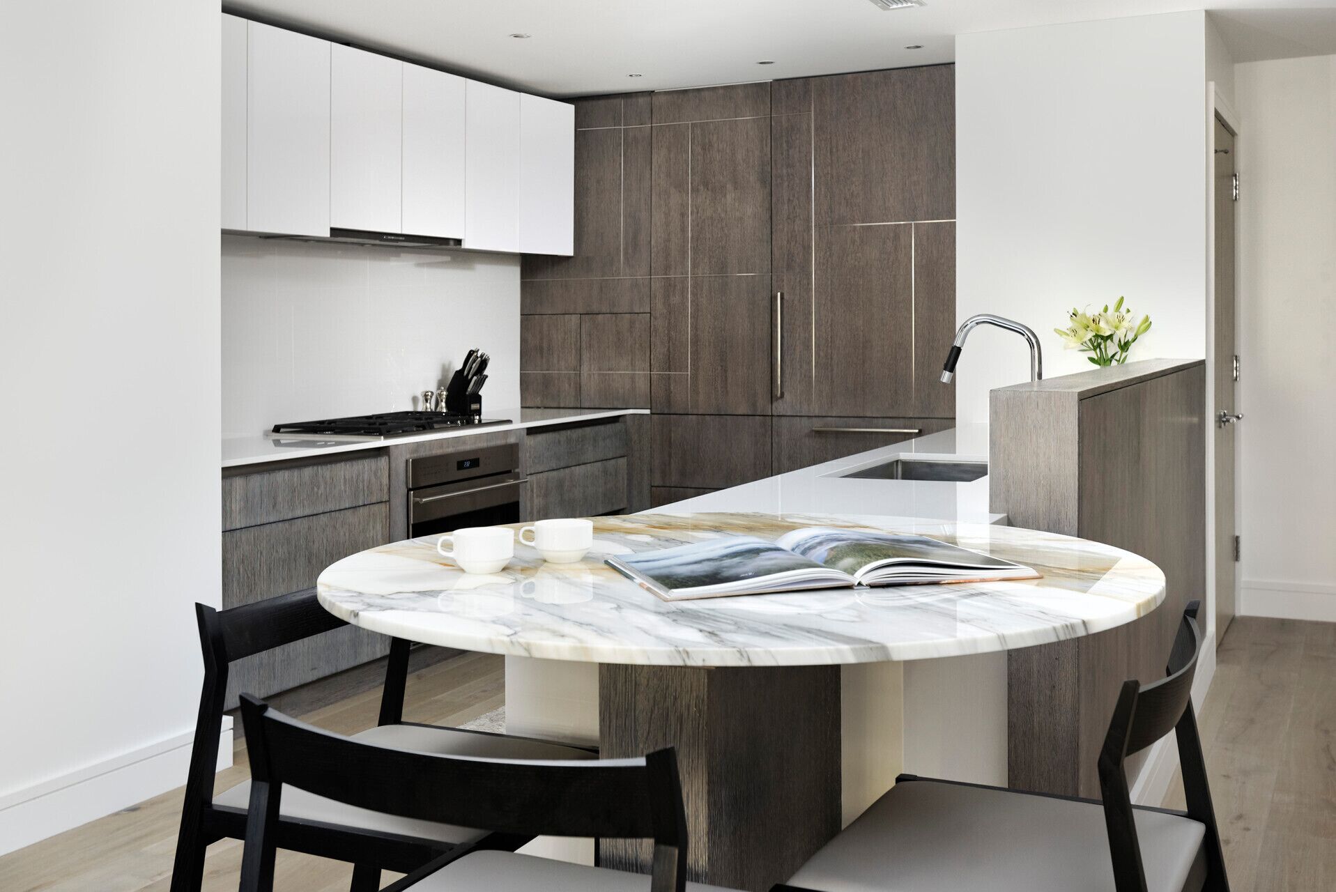 A modern kitchen with a marble island, dark wood cabinetry, and a built-in oven.