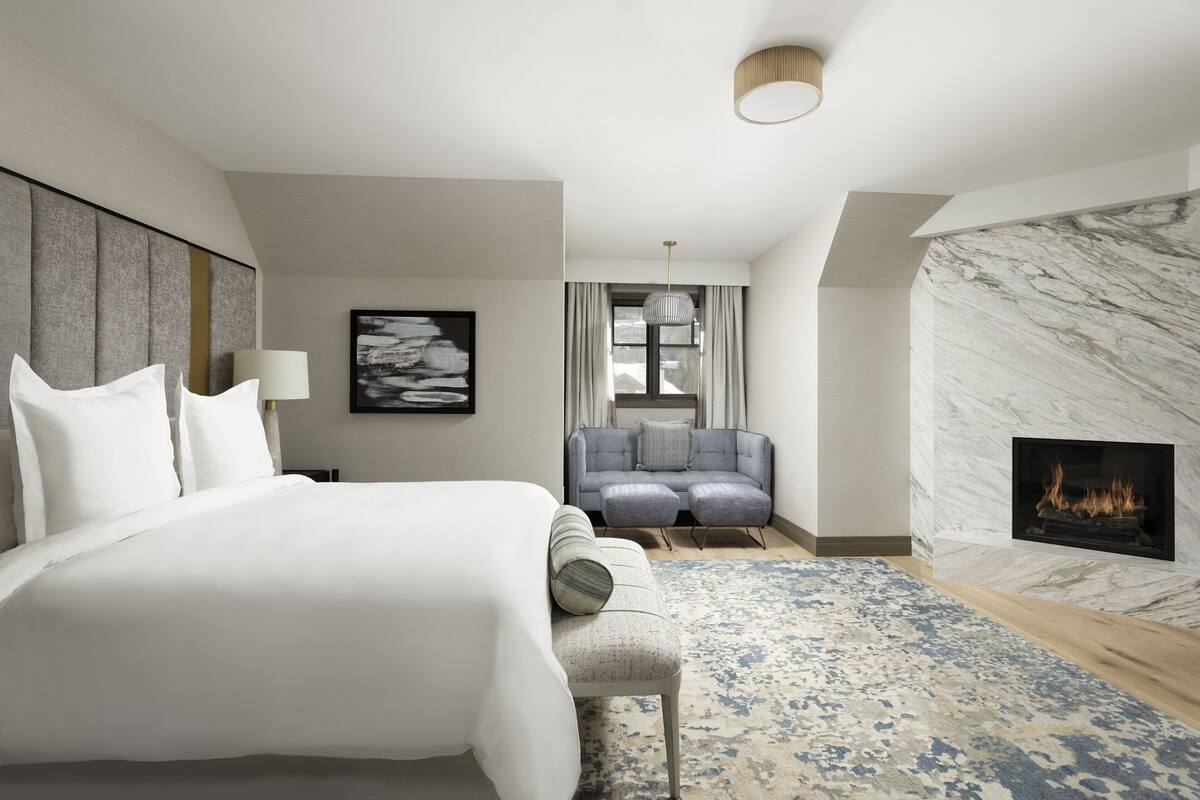 Ein modernes Hotelzimmer mit einem großen Bett, einem Kamin, einer Sitzecke und Blick auf die Stadt.