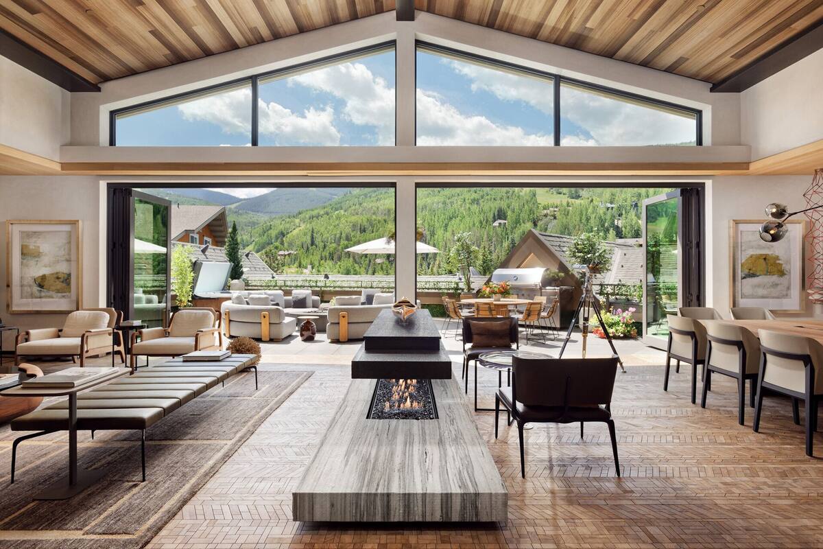 Ein geräumiger Wohnbereich mit Kamin, bequemen Sitzgelegenheiten und großen Fenstern mit Blick auf die Berge.