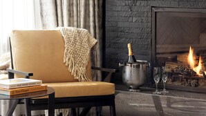 A cozy living room with a leather armchair, a fireplace, a book, and a bottle of champagne.