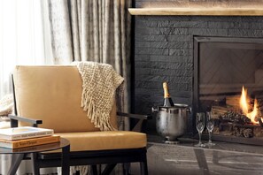 A cozy living room with a leather armchair, a fireplace, a book, and a bottle of champagne.