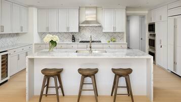 A modern kitchen with white cabinetry, a marble countertop, a central island with stools, and stainless steel appliances.