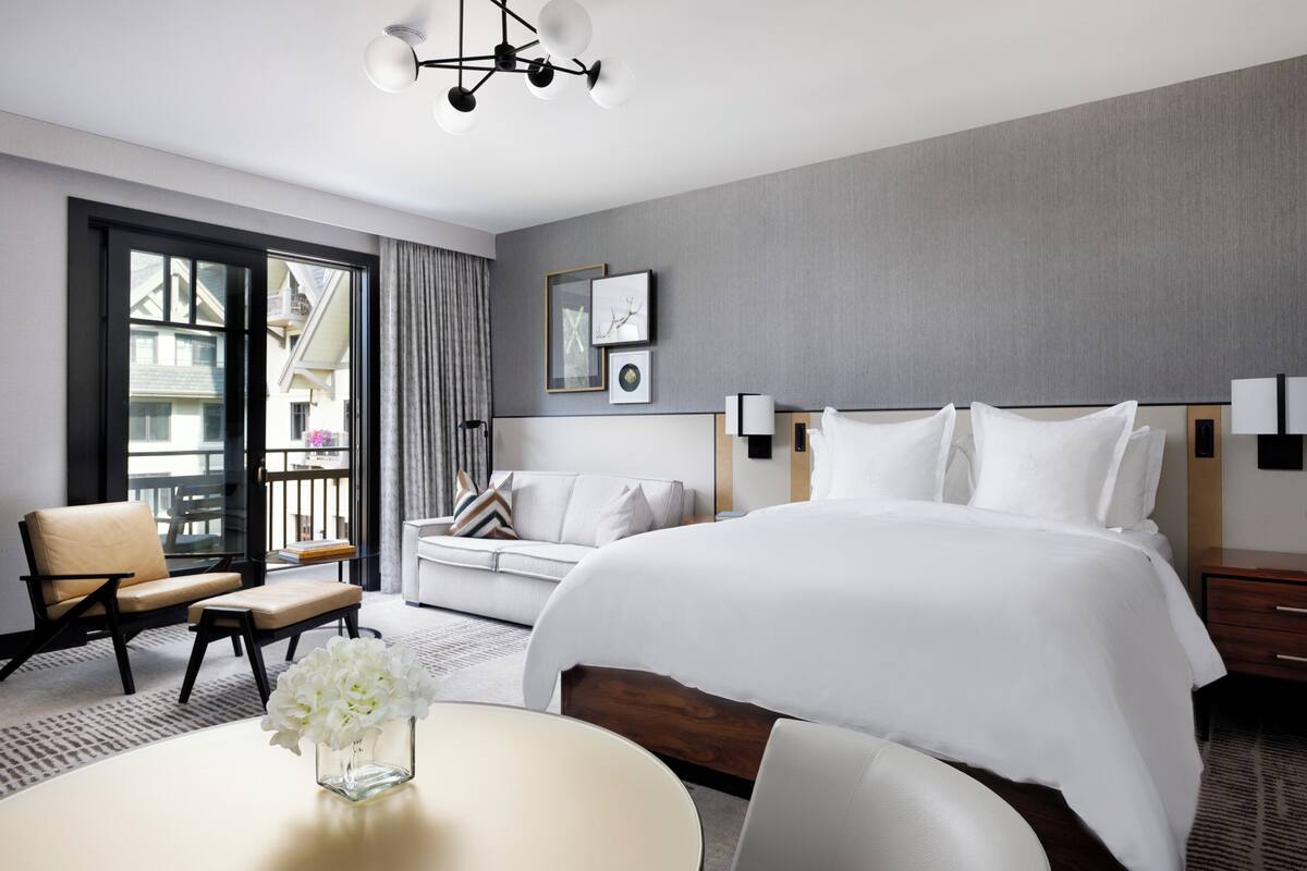 Ein Hotelzimmer mit einem großen Bett, einem Schlafsofa, einem Sessel, einem Tisch mit Blumen und einem Balkon mit Blick.