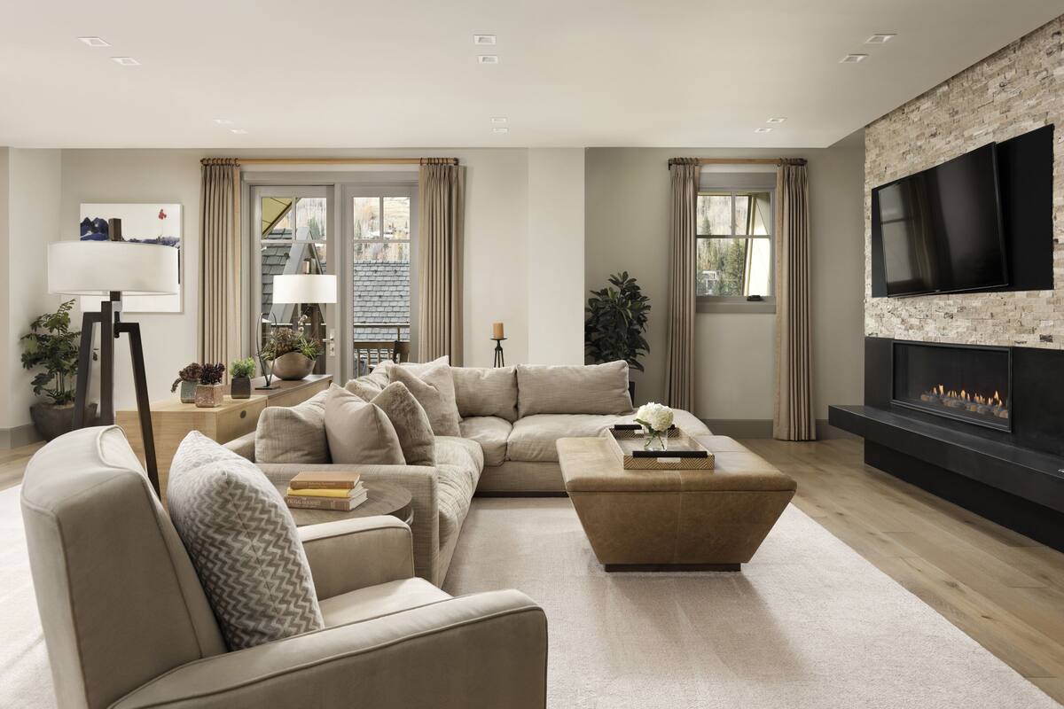 Ein modernes Wohnzimmer mit einem Ecksofa, einem Kamin, einem Flachbildfernseher und großen Fenstern mit Vorhängen.