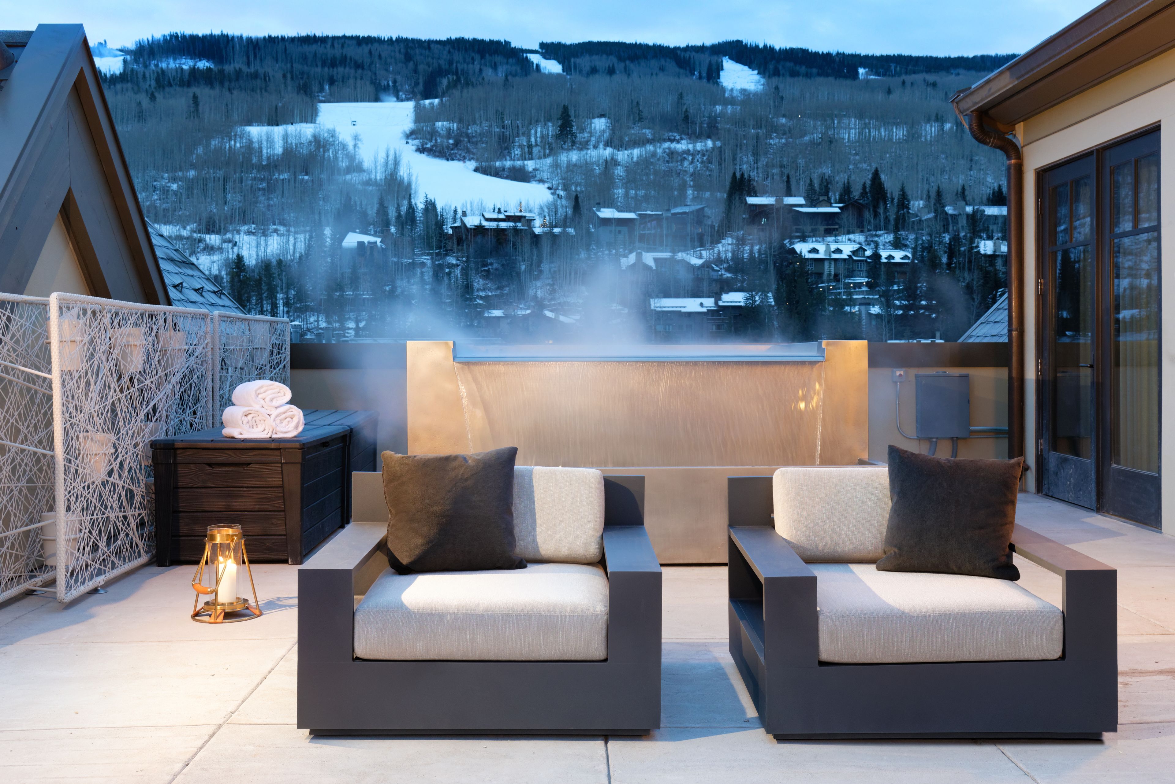 Un espace extérieur moderne aménagé avec deux canapés et une petite table, offrant une vue sur un paysage montagneux enneigé.