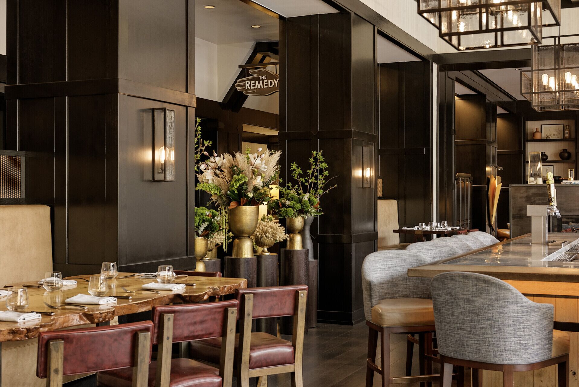 Interior moderno de restaurante con paneles de madera oscura, zona de bar y disposición de mesas para los clientes.