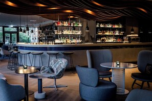A bar area with multiple seating options, a bar counter with shelves of bottles, and a modern ceiling design. - Motel One Hamburg-Alster (Hamburg)