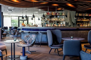 A modern bar area with round tables, bar stools, and a variety of bottles on shelves. - Motel One Hamburg-Alster (Hamburg)