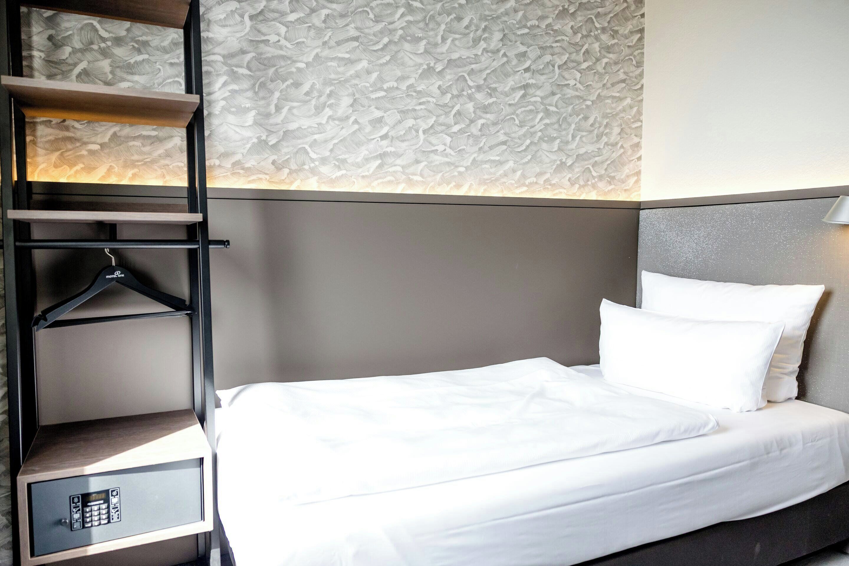 Une chambre d’hôtel avec un lit, une armoire avec une tringle pour suspendre les vêtements et un mur à motifs.