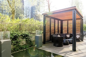 A covered outdoor seating area with a pool, surrounded by greenery and a cityscape. - Motel One Hamburg-Alster (Hamburg)