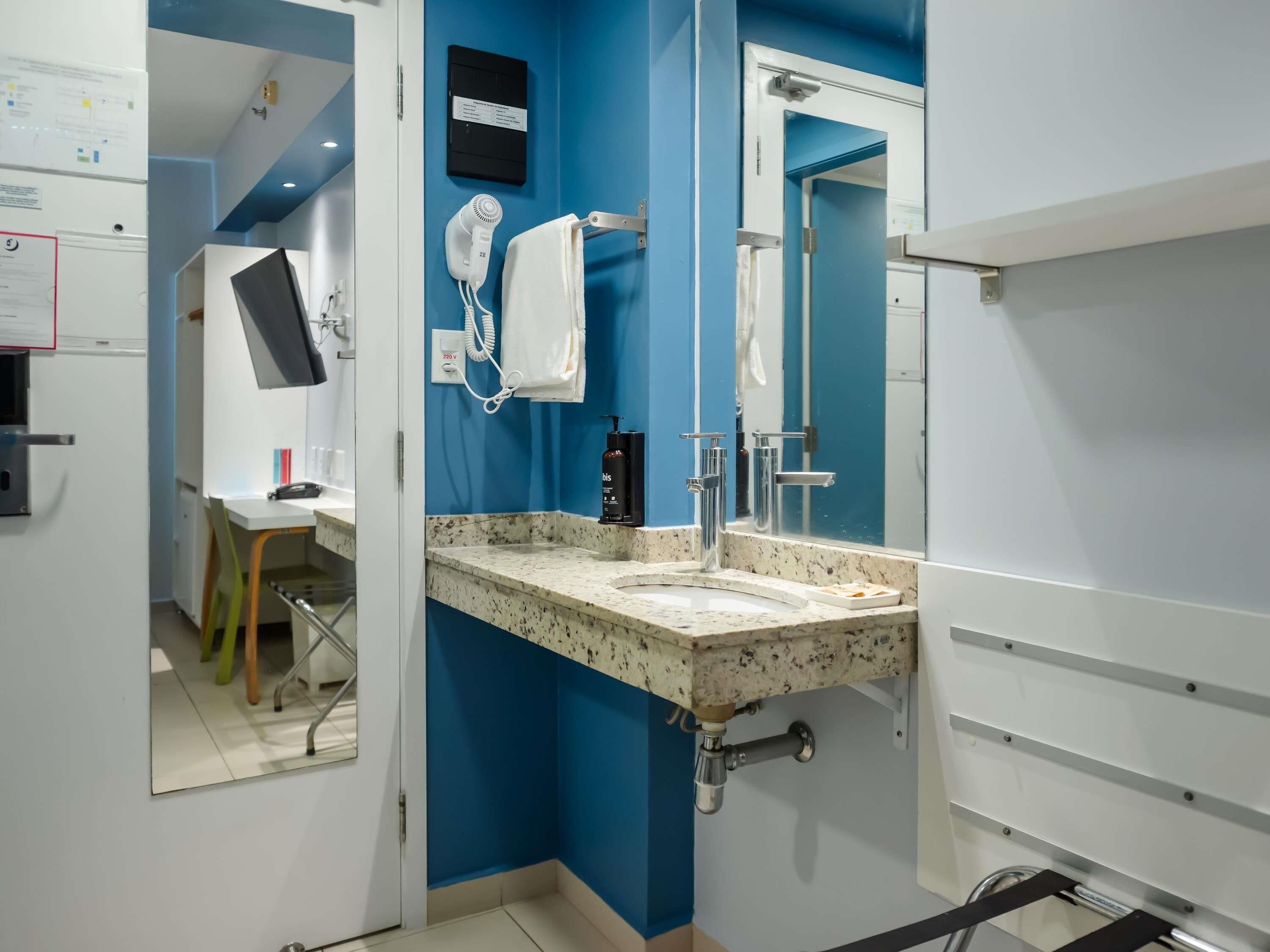 A modern bathroom with a blue accent wall, a sink with a granite countertop, a hairdryer, and a mirror.