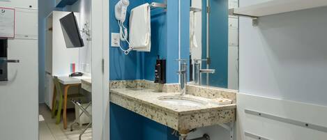 A modern bathroom with a blue accent wall, a sink with a granite countertop, a hairdryer, and a mirror.