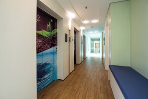 Un pasillo con suelo de madera, un banco azul y una pared con un mural de una planta y una ola.