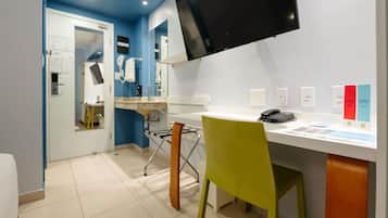 A hotel room with a desk, chair, flat-screen TV, and a mirror.