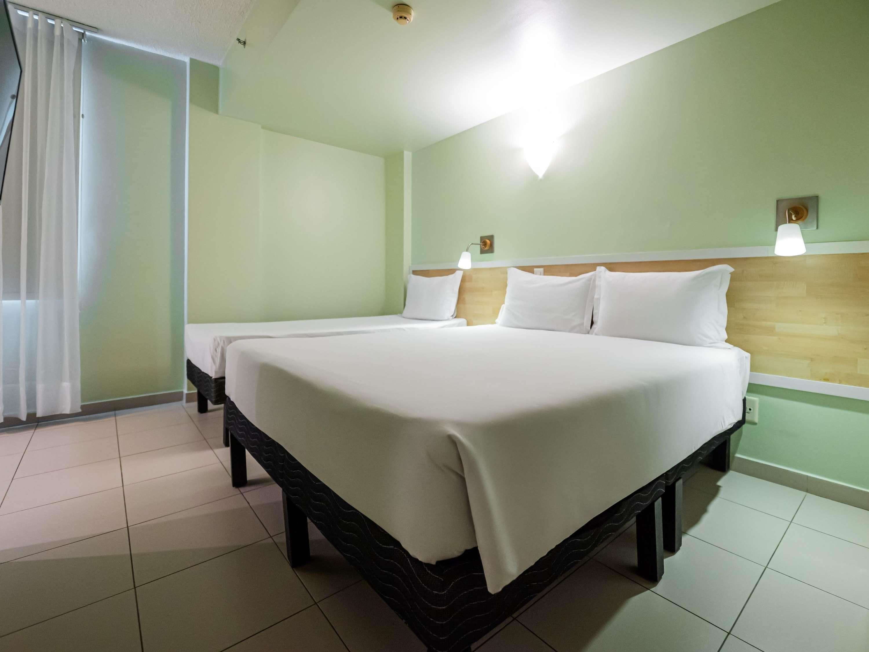 A hotel room with a large bed, a wooden headboard, and a window with curtains.
