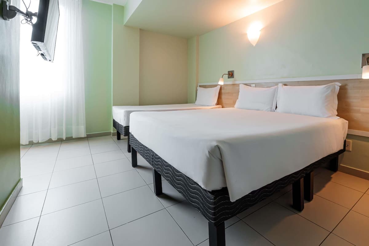 A hotel room with two beds, a TV mounted on the wall, and a ceiling light fixture.