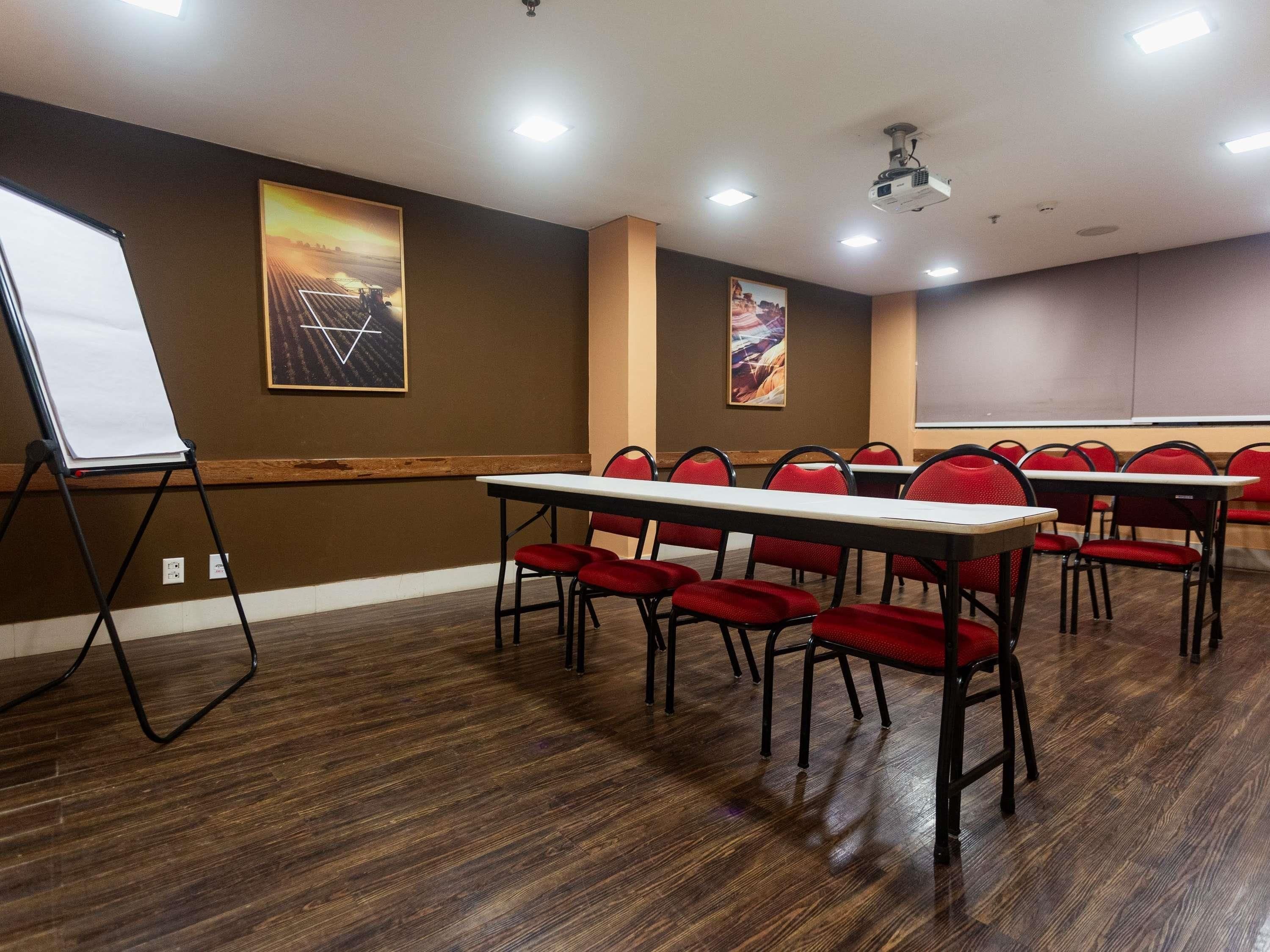 A conference room with a long table, red chairs, a whiteboard, and two paintings on the walls.
