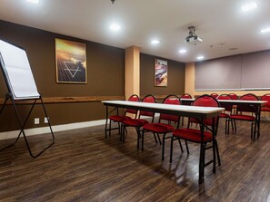 A conference room with a long table, red chairs, a whiteboard, and two paintings on the walls.