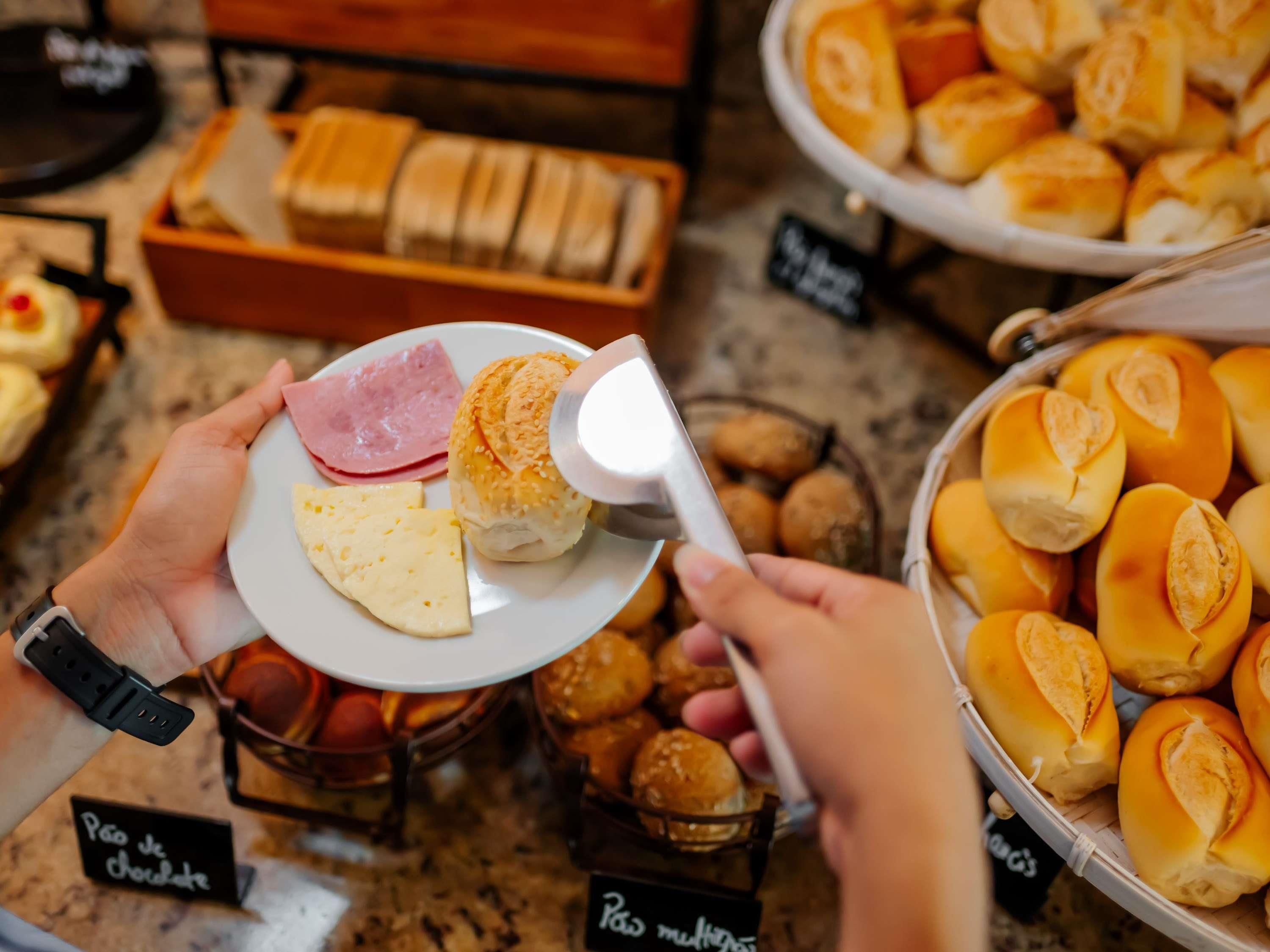 Una persona sosteniendo un plato con queso y jamón, y un pastel en el fondo.