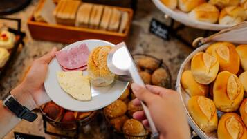 Una persona sosteniendo un plato con queso y jamón, y un pastel en el fondo.