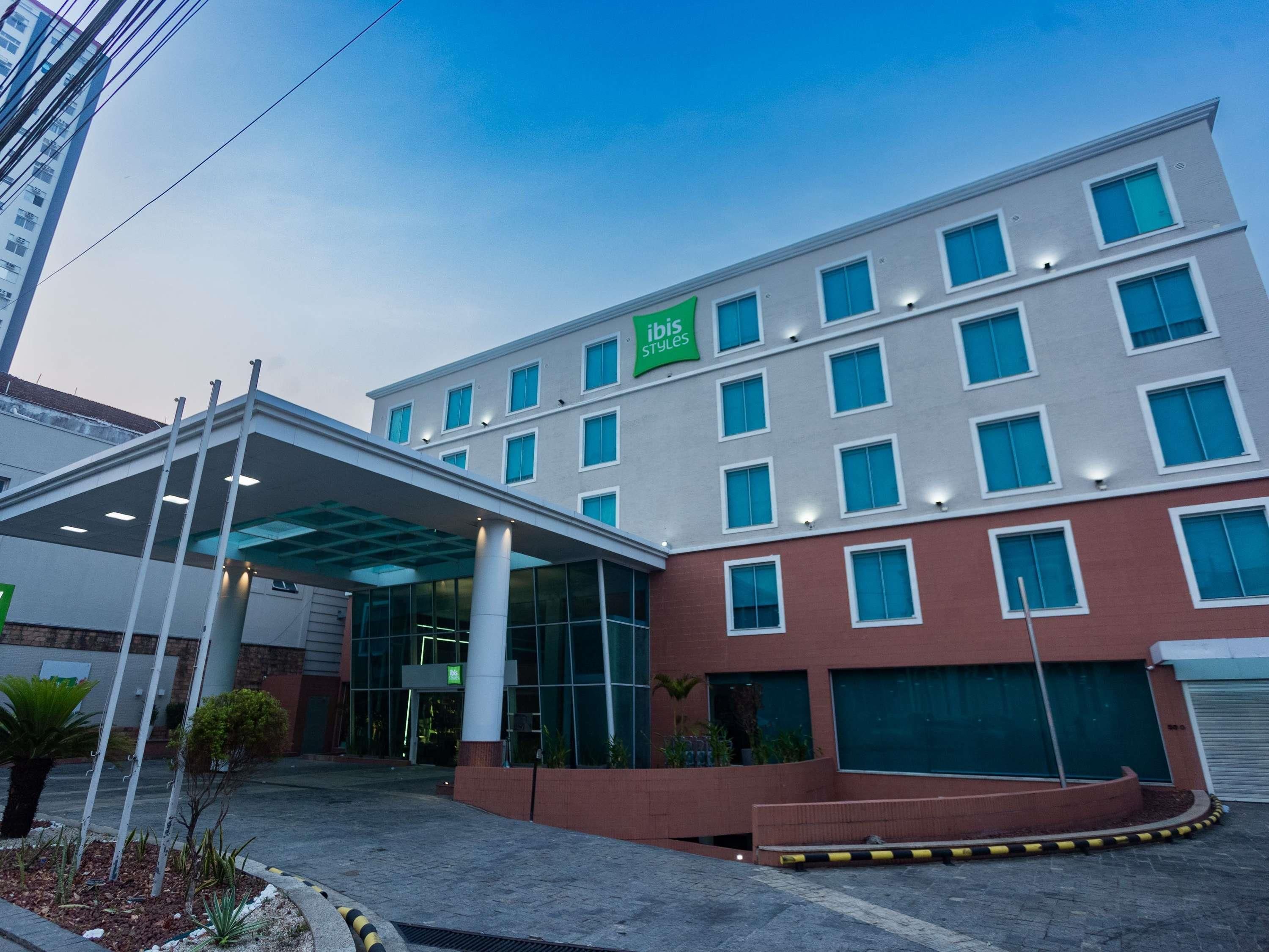 Um hotel moderno com vários andares, com entrada coberta e uma placa verde destacada.