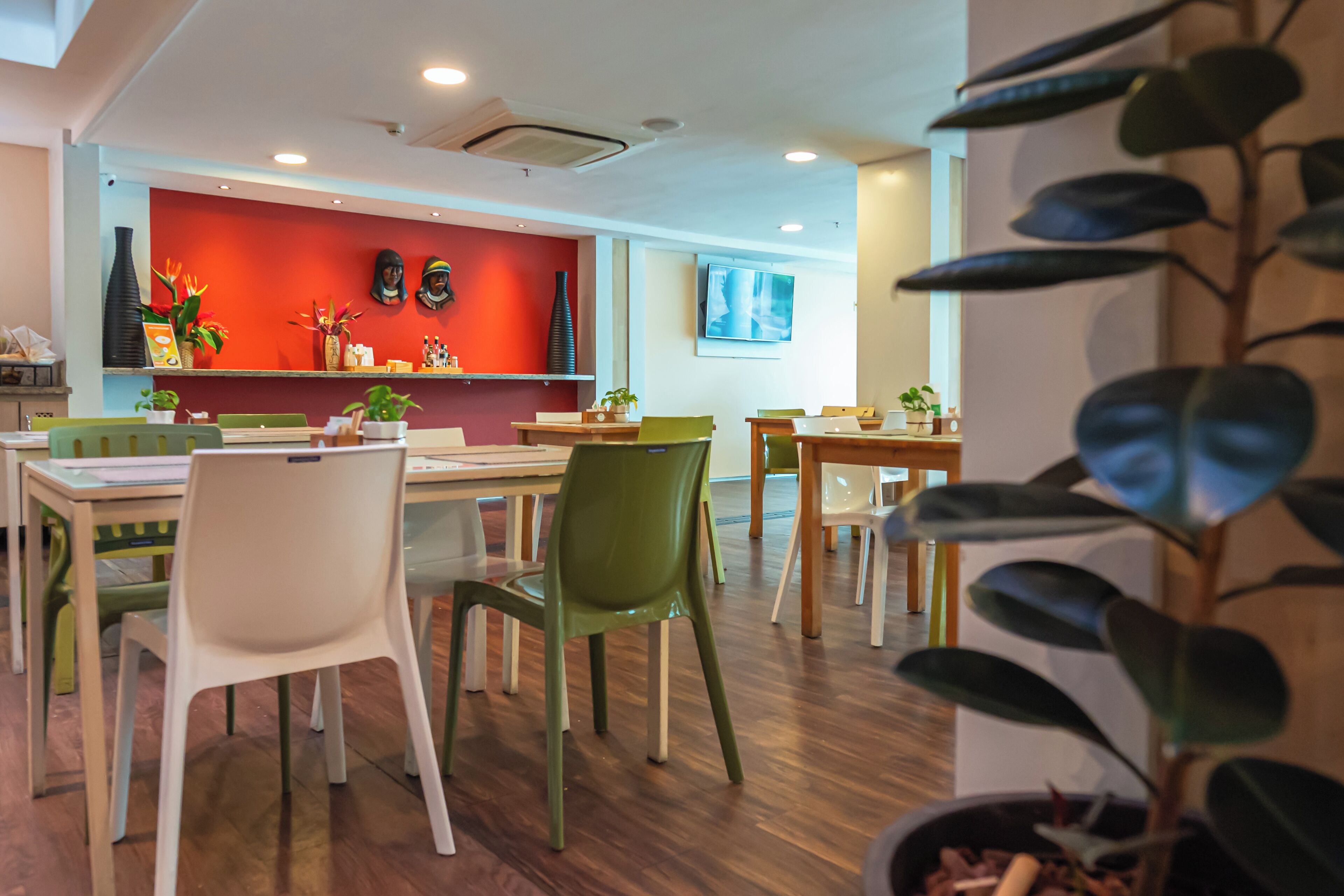 Un comedor moderno con mesas y sillas de madera, una pared de acento roja y plantas en macetas.