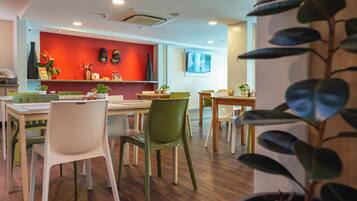 Un comedor moderno con mesas y sillas de madera, una pared de acento roja y plantas en macetas.