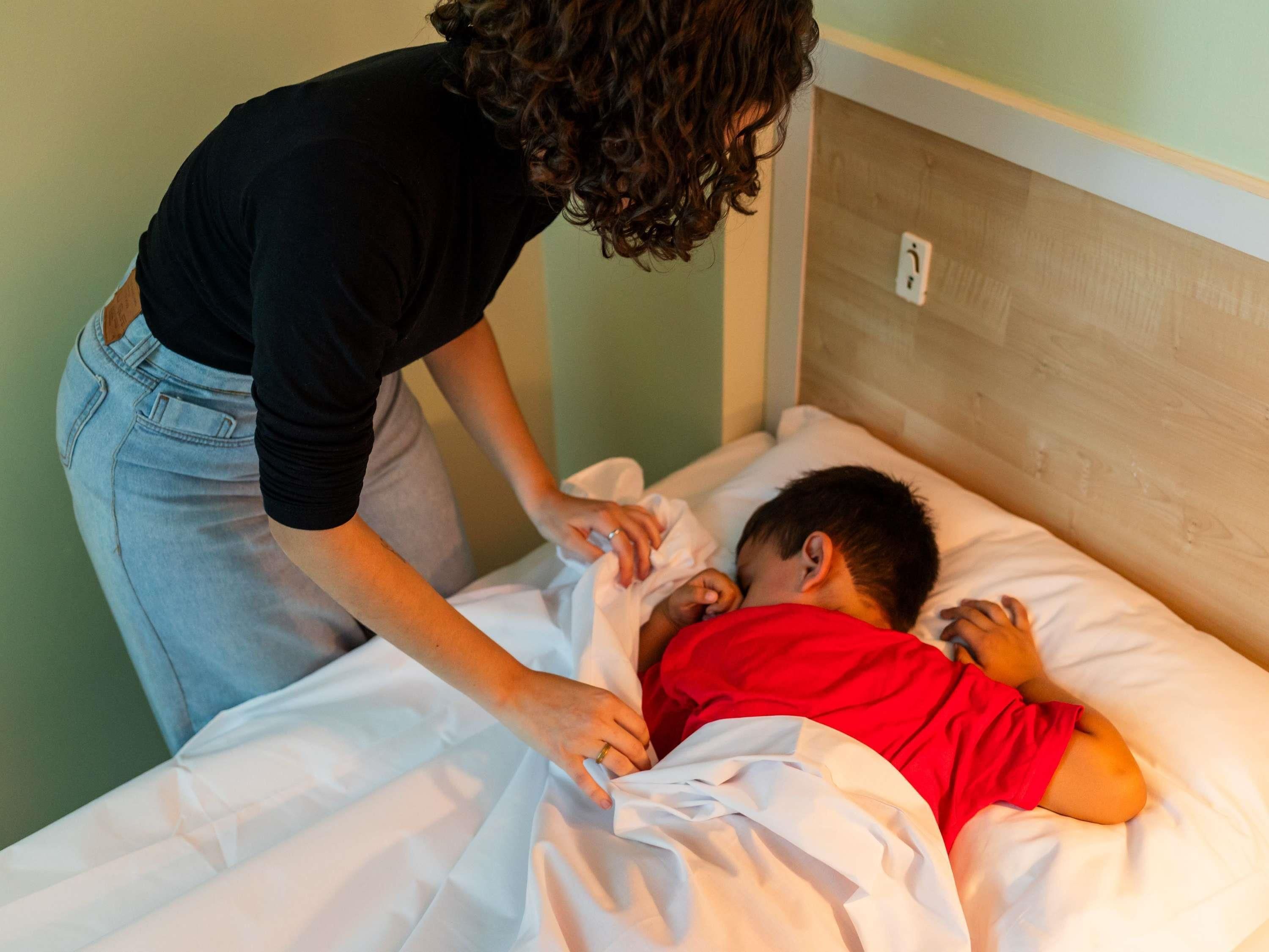 A person adjusting a bed with a child in a red shirt.