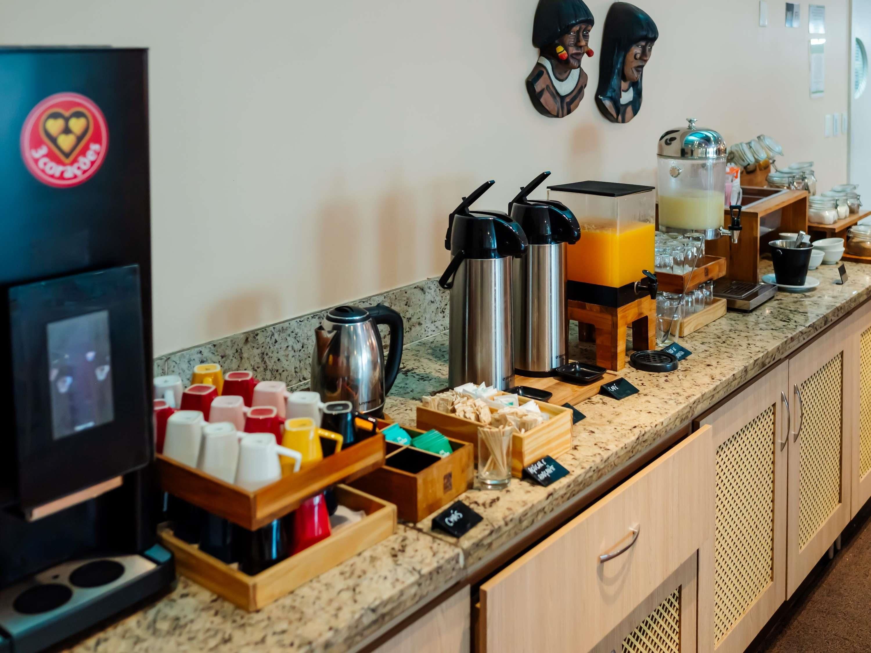 Una barra de desayuno con máquinas de café, dispensador de zumo y diferentes condimentos.