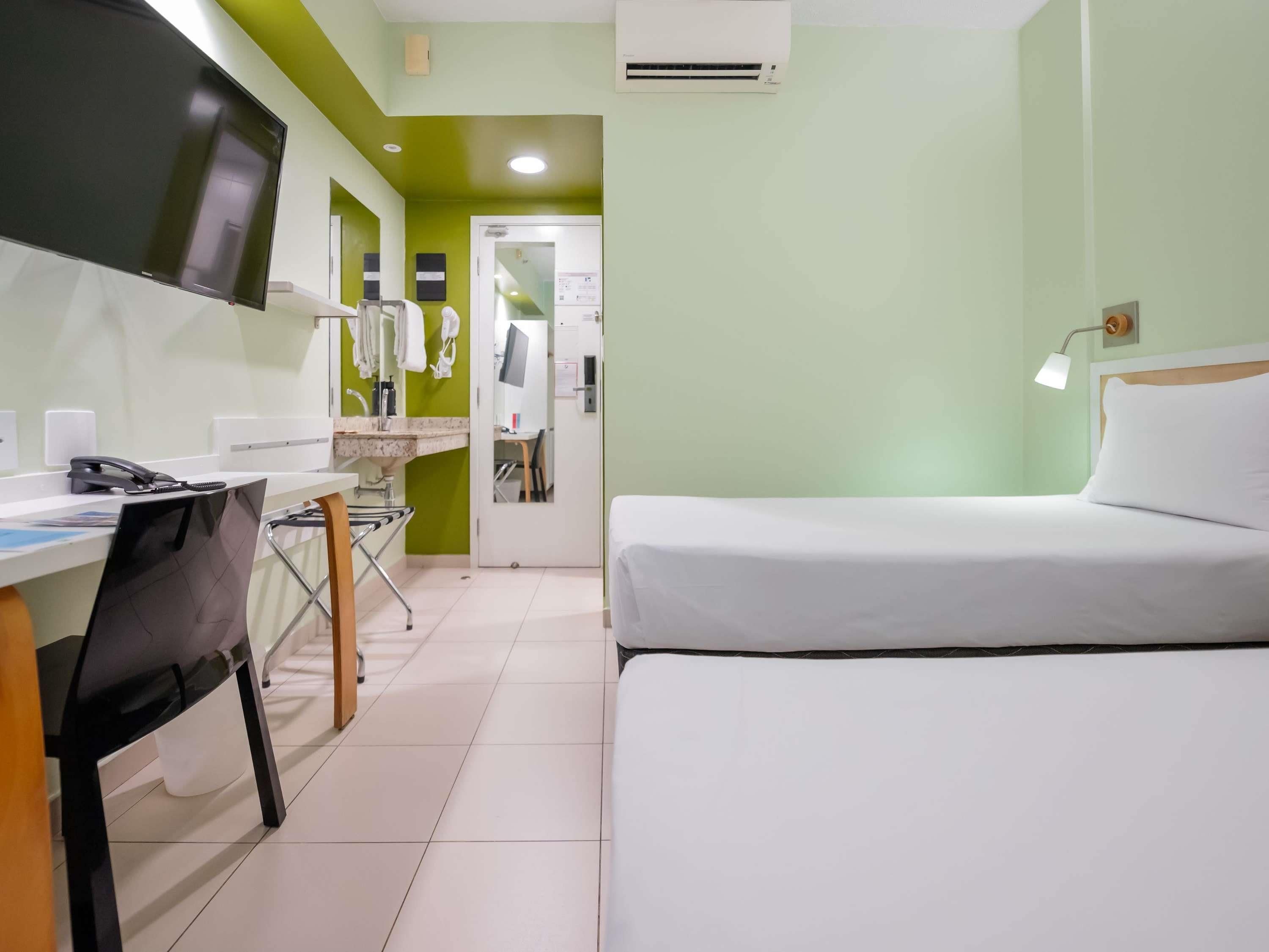 A hotel room with a bed, a desk with a computer, a chair, and a TV.