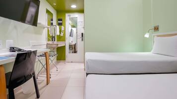 A hotel room with a bed, a desk with a computer, a chair, and a TV.