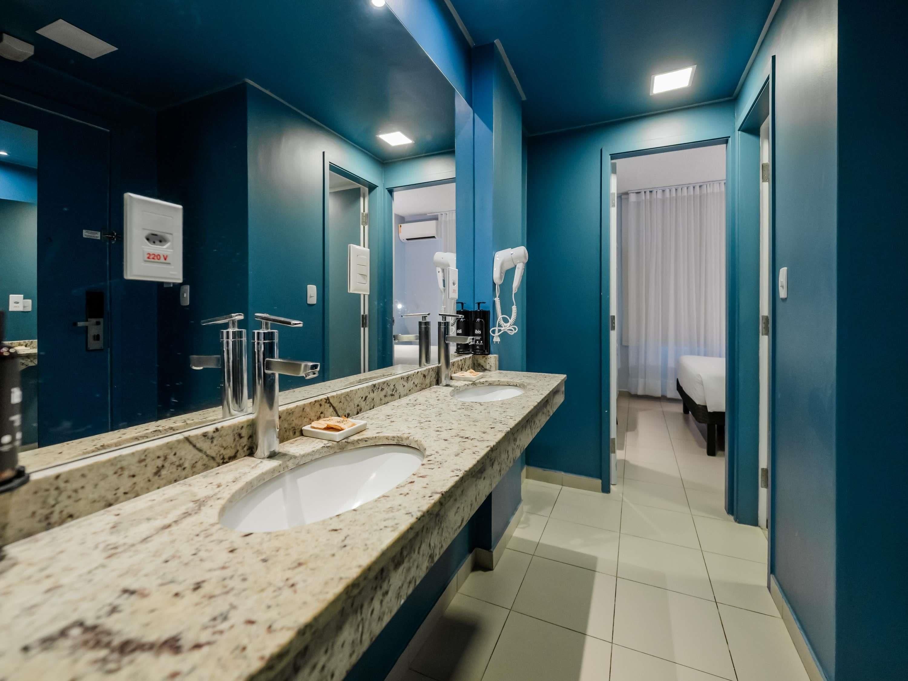 A modern bathroom with three sinks, a hairdryer, and a mirror.