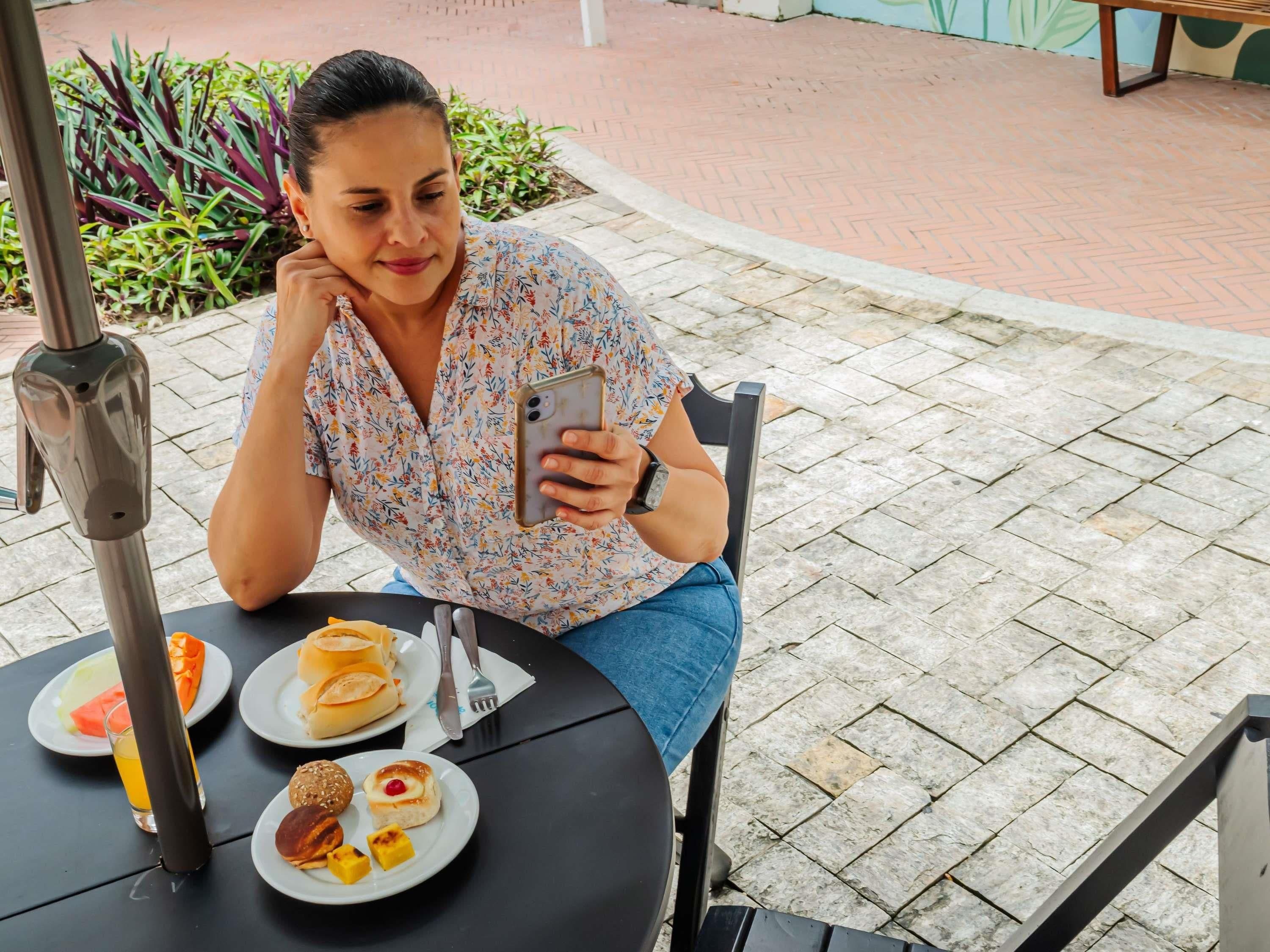 A person seated at an outdoor table with a meal, a water bottle, and a smartphone.