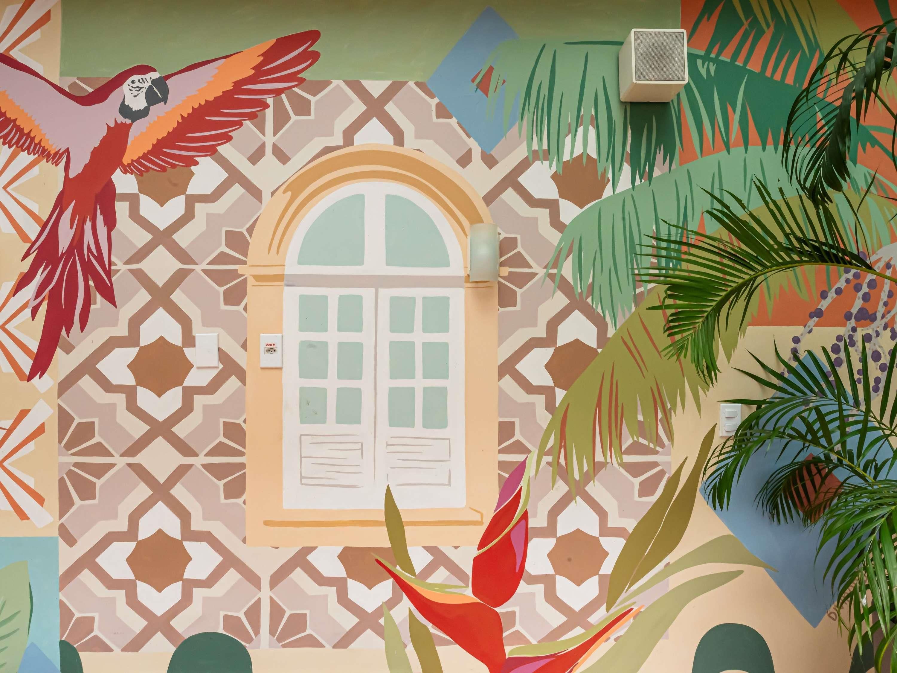 A room with a patterned wall, a window with shutters, a wall socket, and a plant.