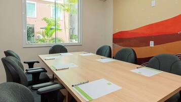 Sala de conferências com uma mesa comprida, seis cadeiras e uma janela com vista para edifícios e áreas verdes.