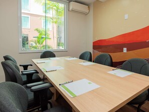 A conference room with a long table, six chairs, and a window with a view of buildings and greenery.