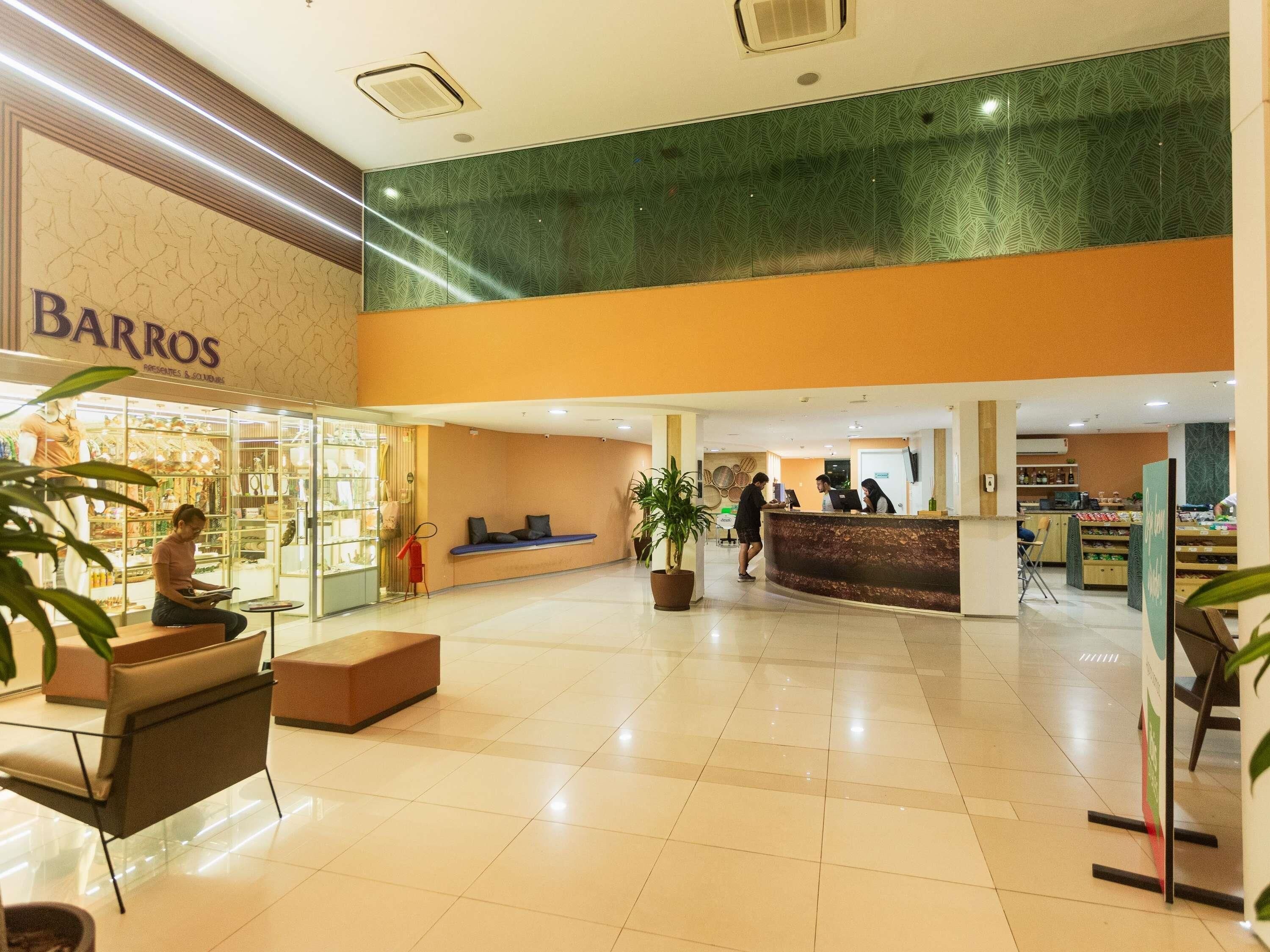 A hotel lobby with a reception desk, seating area, and a store named 'Barros'.