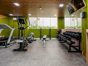Un gimnasio con máquinas de cardio, pesas sueltas y un espejo grande.