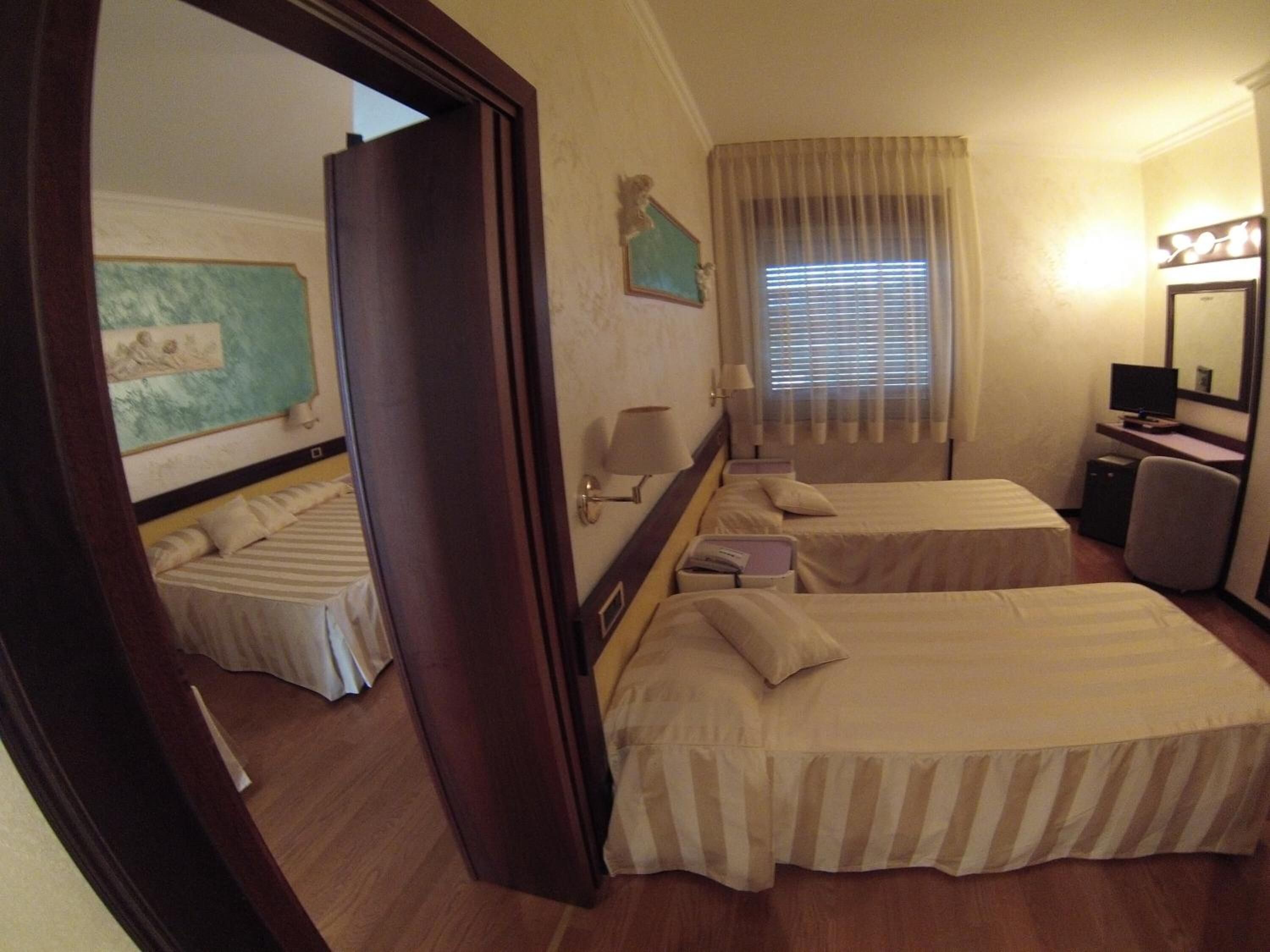 A hotel room with two beds, a desk with a computer, a mirror, and a window with curtains.