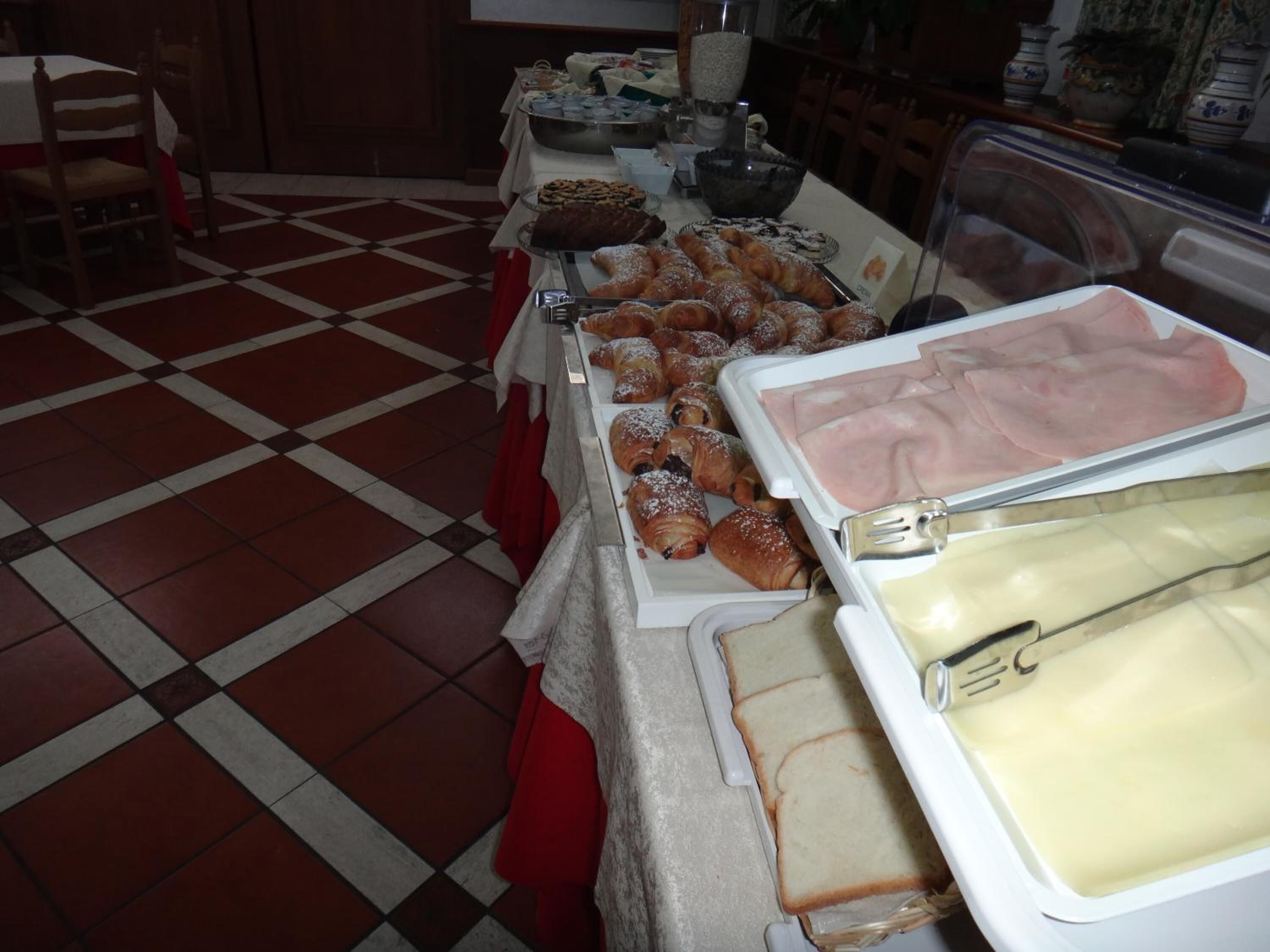A buffet table with various food items including pastries, bread, and deli meats.