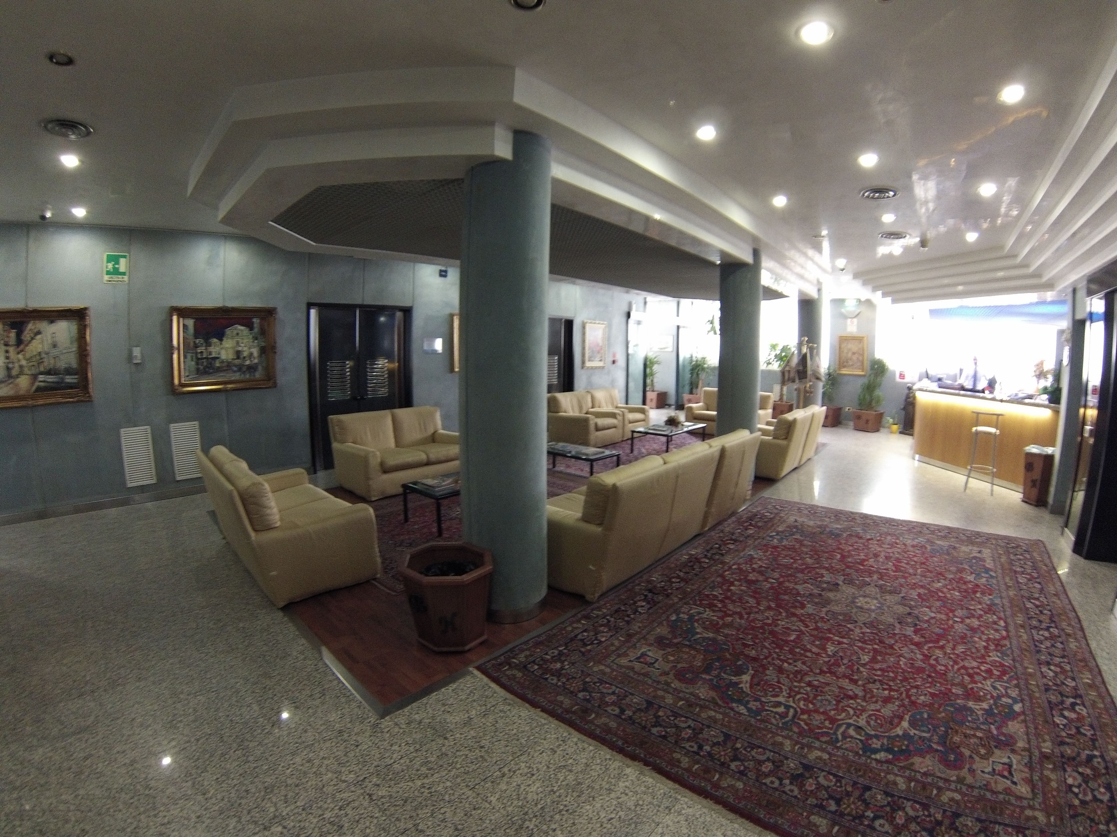 En rummelig lobby med beige sofaer, et stort mønstret tæppe og en receptionsdisk.