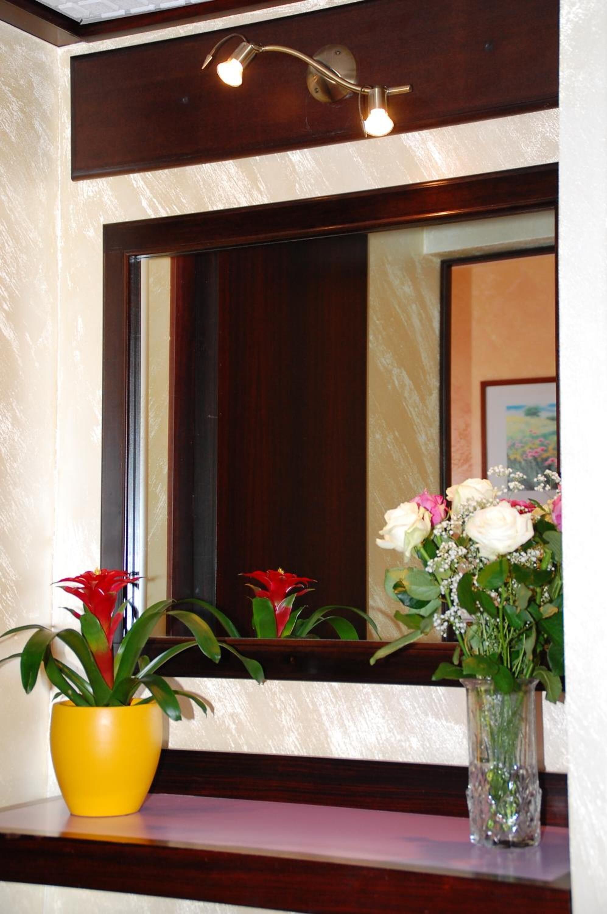 Un miroir avec un cadre en bois, un vase jaune avec des fleurs rouges et un vase transparent avec des fleurs blanches et roses.