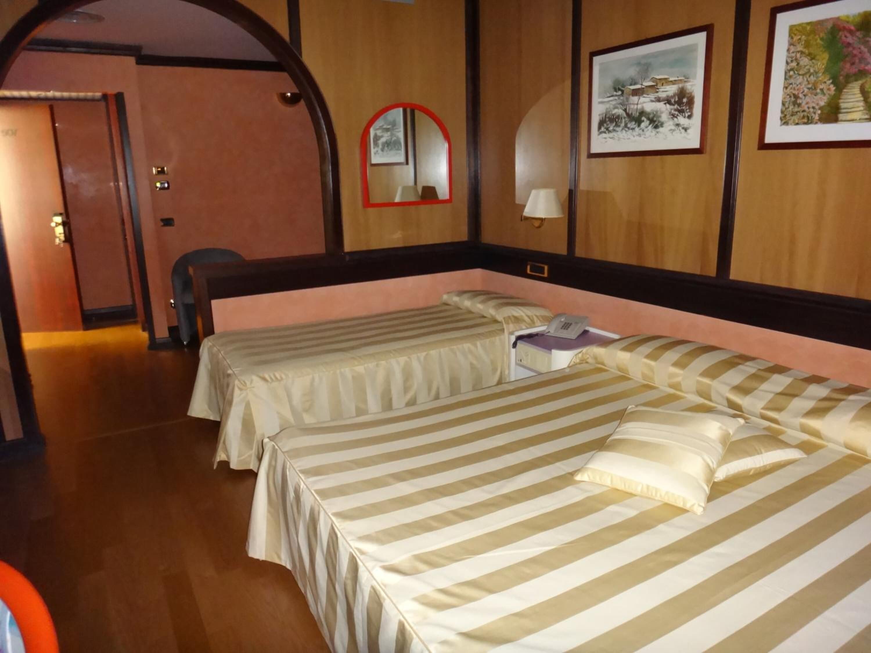 Una camera d'albergo con due letti, uno specchio e quadri appesi al muro.