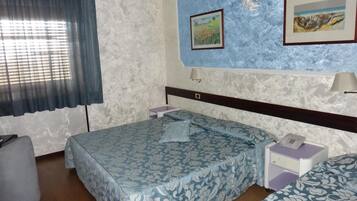 Ein Hotelzimmer mit einem Bett, einem Nachttisch mit Lampe, einem kleinen Tisch mit Telefon und einem Fenster mit Vorhängen.